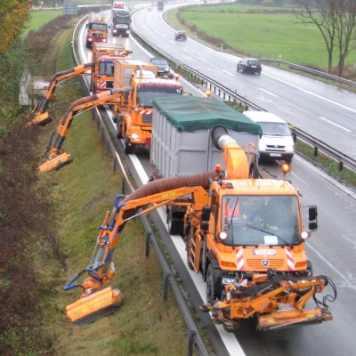 Drei Mähfahrzeuge mähen hinter der Autobahn-Leitplanke